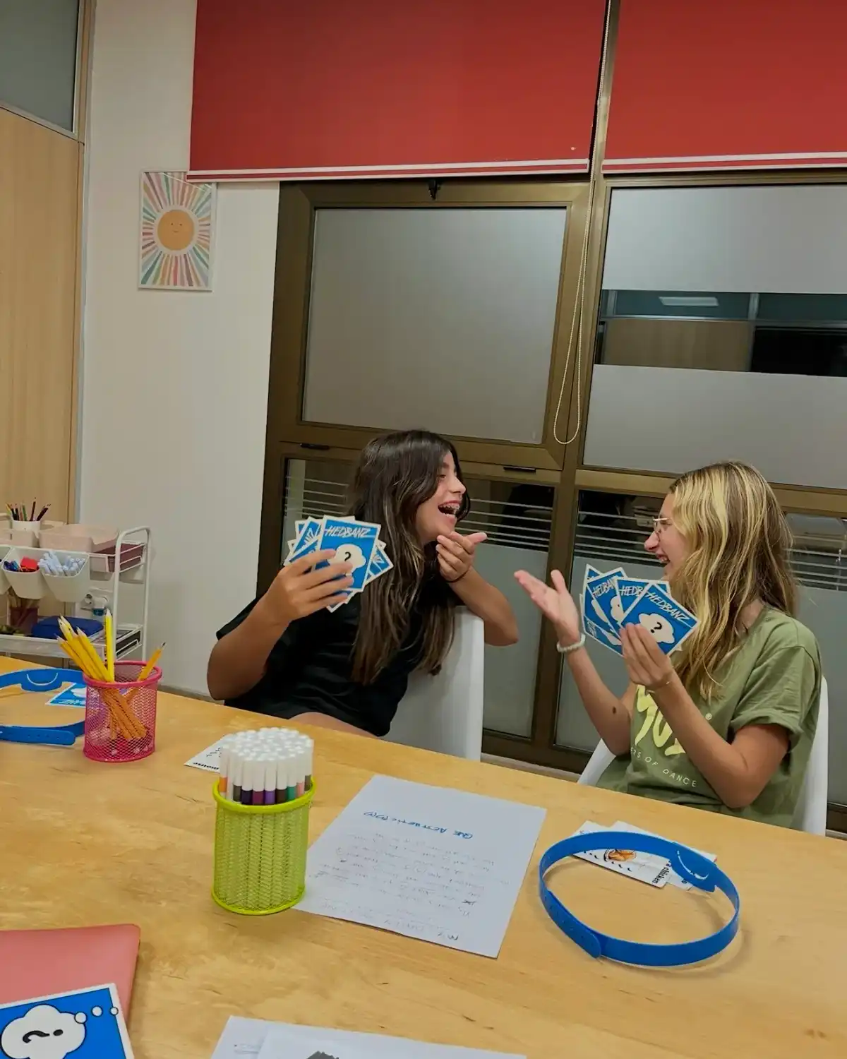Dos adolescentes se ríen jugando a un juego de cartas de preguntas en inglés