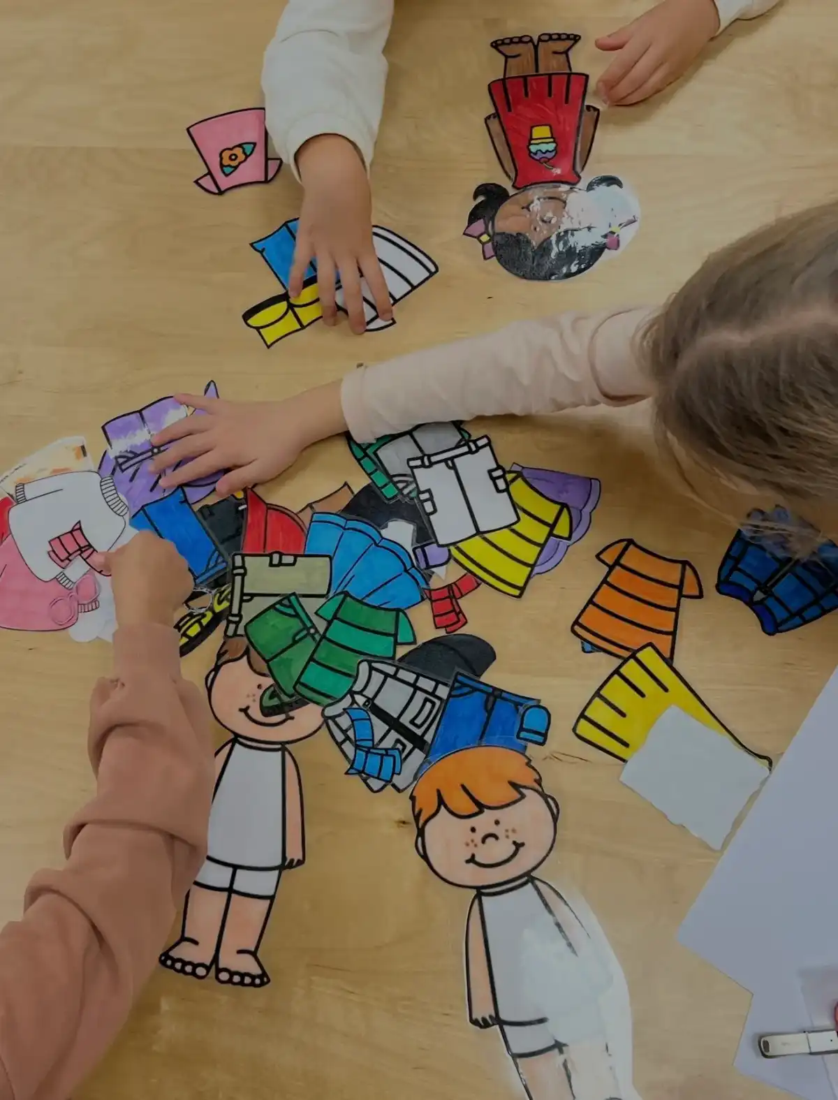 Niños vistiendo muñecos de papel con ropa recortada